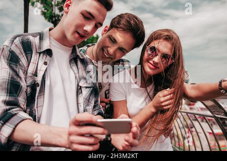 Drei Beste Freunde, Die Fotos Auf Dem Mobiltelefon Im Freien Ansehen. Stockfoto