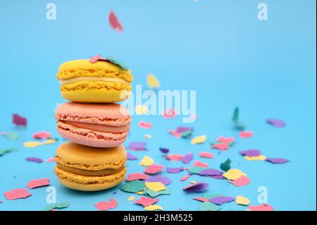 Bunte Macarons auf trendigem pastellblauem Papier mit Konfetti. Leckere rosa, gelbe und braune Makronen. Stockfoto