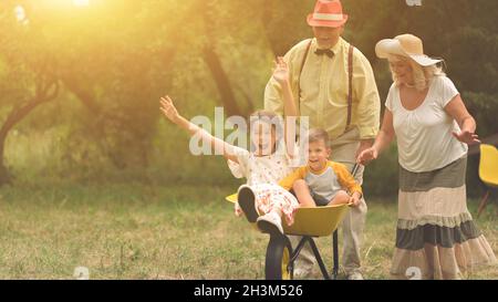 Oma und Opa drängen ihre Enkel in Eine Schubkarre Stockfoto