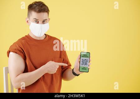 Lächelnder, hübscher junger Mann, der mit QR-Code auf dem Bildschirm auf das Smartphone zeigt Stockfoto