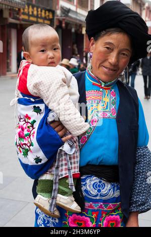 Frau in traditionellen tibetischen Kleidern mit Baby/Kleinkind, wahrscheinlich mit ihrem Enkelkind: Tibeterin/ethnische Frauen, wohnhaft oder ortsansässig in der alten chinesischen Stadt (alte ummauerte Stadt) von Songpan im Norden von Sichuan, China (125) Stockfoto