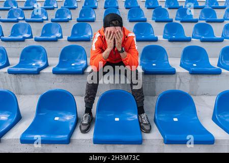 Enttäuscht verärgert junger Fan sitzt auf der Tribüne. Fan ist enttäuscht über den Verlust seiner Lieblings-Team. Eine Person im Stadion. Stockfoto