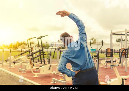 Ein Mann in einem Geschäftsanzug wärmt sich auf Simulatoren im Stadion auf. Sportübungen nach der Büroarbeit. Der Kampf gegen Übergewicht. Geschäftsmann Stockfoto