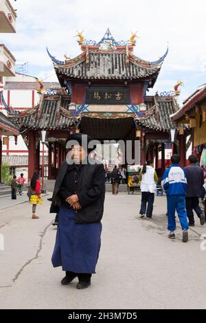 Tibetische Frau vor der Tongyuan-Brücke überdachter Gang im Stil einer Pagode mit abgestufter Dachkonstruktion und mehreren Dachrinnen. Songpan ist eine Stadt in der nördlichen Provinz Sichuan, China. (125) Stockfoto