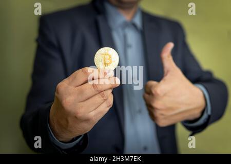 Geschäftsmann hält Kryptowährung Bitcoin. Glücklich und positiv, Daumen nach oben tun hervorragende und Zustimmung Zeichen. Gewinn- und Umsatzeinfall durch Bitcoin Tradi Stockfoto