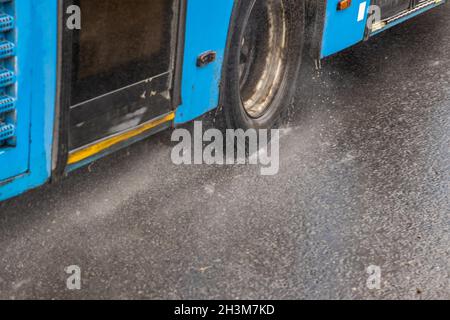 Blauer Stadtbus, der auf einer regnerischen Straße mit Wasserspritzern fährt Stockfoto