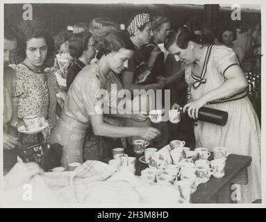 Ein Vintage-Foto um den Februar 1942, auf dem eine Frau auf der Ipoh Station in Perak, Malaysia, Tee für eine Gruppe von Flüchtlingsfrauen aus Penang auf dem Weg nach Singapur während der japanischen Invasion in Malaya goss Stockfoto