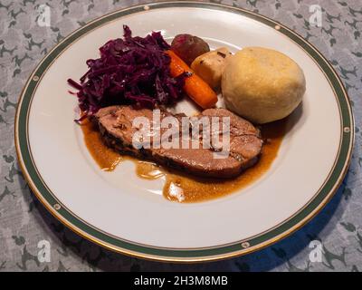 Ein Stück gebratenes Jungschweinferkelchen mit Rotkohl, Kartoffelknödel, Wintergemüse und Soße Stockfoto