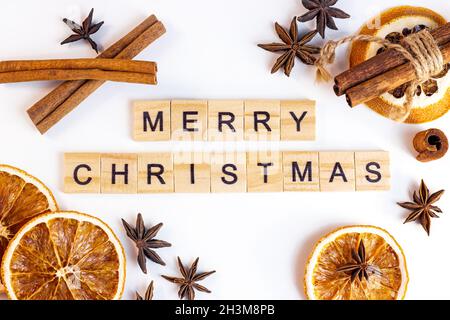 Draufsicht flache Holzlage Frohe Weihnachtstexte mit Gewürzen für traditionelle Getränke: Zimtstangen, Anissterne, trockene Orangenscheiben zur Weihnachtszeit Stockfoto