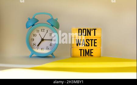 Verschwenden Sie keine Zeit, die auf Holzblöcken auf einem hellen Hintergrund neben einem Wecker geschrieben ist. Stockfoto