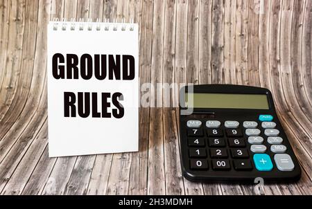 Der Text GRUNDREGELN ist auf einem Notizbuch geschrieben, daneben liegt ein Caddy Rechner auf einem hölzernen Stockfoto