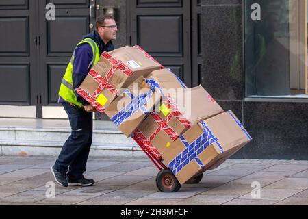 Zustelltreiber, der Pakete für den Office Store zustellt. Lieferwagen für trendige Schuhketten, die Schuhe von Eigenmarken und Marken verkaufen, Verkaufslager für schwere, zweirädrige Sackkarren auf Rädern. Preston, Großbritannien Stockfoto