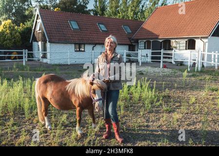 Porträt einer lächelnden älteren Frau, die mit einem Pony auf dem Bauernhof steht Stockfoto