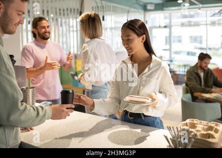 Mann, der Kaffee zum Mitnehmen und süßes Dessert in einem modernen Café der glücklichen asiatischen Frau serviert Stockfoto