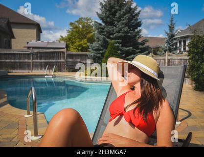 Frau in rotem Bikini und Sonnenhut, die im Sommer am Pool faulenzt. Stockfoto