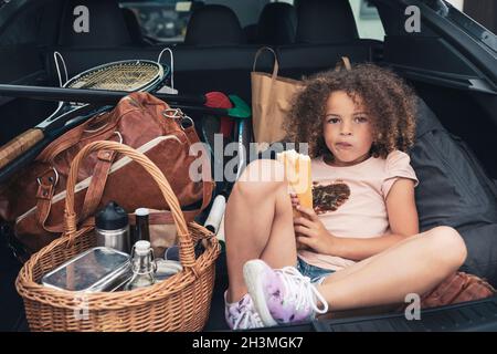 Porträt eines Mädchens, das Brot isst, während es mit Gepäck im Kofferraum sitzt Stockfoto