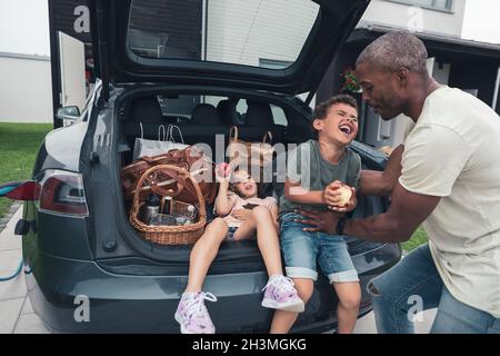 Vater kitzelt Sohn sitzt von Mädchen im Kofferraum auf dem Vorgarten Stockfoto