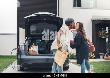 Heterosexuelles Paar, das sich küsst, während es neben einem Elektroauto steht Stockfoto