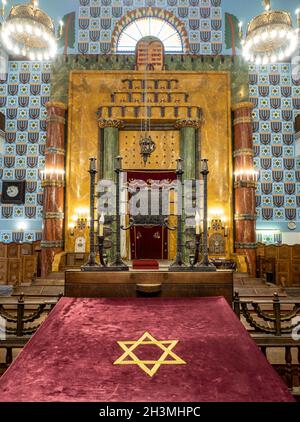 Vorderseite der orthodoxen Synagoge von Kazinczy: Die hoch dekorierte Vorderseite dieser antiken Synagoge mit dem ewigen Licht, dem Kerzenleuchter, der Bimah und der Arche. Eine mit Teppich ausgelegte Plattform mit einem Davidstern steht im Vordergrund. Stockfoto