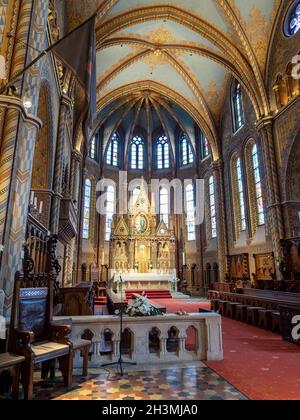 Chior und Altar in der Mathias-Kirche: Umrahmt von hohen goldenen Säulen und hell erleuchteten Buntglasfenstern leuchtet der goldene Altar im warmen Stockfoto