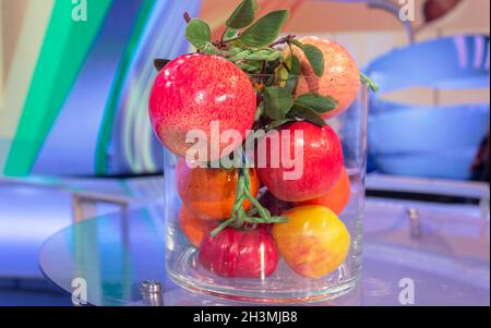 Orangen, Zitronen und Äpfel in einer großen Glasvase auf buntem Hintergrund Stockfoto