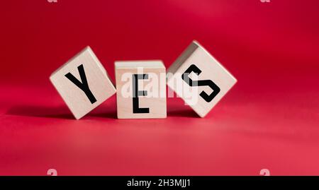 Das Wort JA steht in schwarzen Buchstaben auf Holzblöcken geschrieben. Buchstabieren Sie die Meldung „Ja“ auf einem roten Hintergrund. Geschäfts-, Motivations- und Bildungskonzept Stockfoto