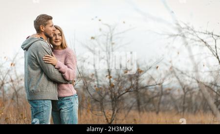 Liebevolles Paar, das sich auf einem Hintergrund der herbstlichen Naturlandschaft ausruhen und umarmen kann. Junge kaukasische Mann und Frau huggin Stockfoto