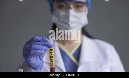 Blutteströhre mit Aufschrift covid-19 in der Hand des Arztes im Vordergrund. Selektiver Fokus auf Reagenzglas mit gelbem Etikett. Cl Stockfoto