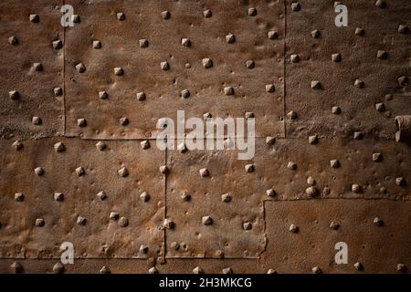 Alte Wand mit rostrosen Eisenblechen mit Nieten bedeckt. Abstrakter Retro-Hintergrund Stockfoto