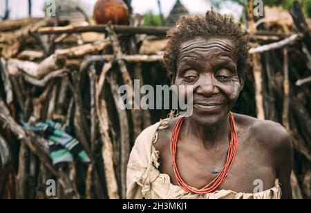 TOPOSA STAMM, SÜDSUDAN - 12. MÄRZ 2020: Alte blinde Frau aus Toposa Stamm steht auf verschwommenem Hintergrund von Stick Hütte in vil Stockfoto