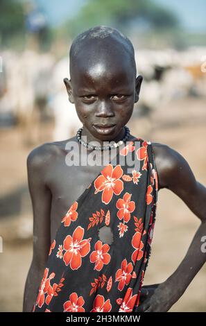 MUNDARI TRIBE, SÜDSUDAN - 11. MÄRZ 2020: Kind in traditionellem Gewand mit floralem Ornament, das die Hand an der Taille hält und ein Stockfoto