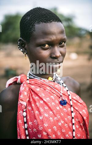 TOPOSA STAMM, SÜDSUDAN - 12. MÄRZ 2020: Teenager mit kurzen Haaren tragen helle Kleidung und Accessoires und Blick auf Camer Stockfoto