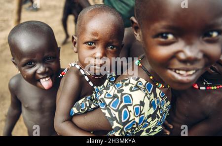 TOPOSA STAMM, SÜDSUDAN - MÄRZ 12, 2020: Mädchen lächelnd und trägt Baby Geschwister auf dem Rücken, während sie mit Freunden im Dorf spielen Stockfoto