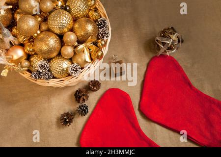 Riesiger Korbkorb gefüllt mit goldenen Bällen und Weihnachts-Weihnachtssocken auf Braun mit Tannenzapfen Stockfoto