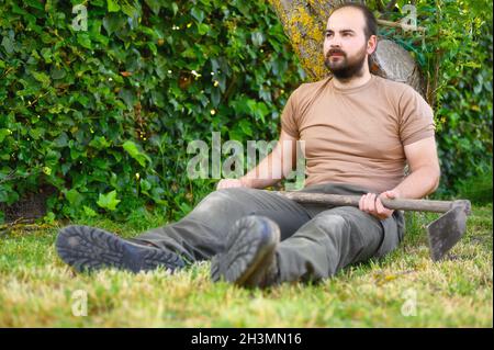 Ein erwachsener Bauer mit einer Hacke, die auf dem Hof ruht. Stockfoto