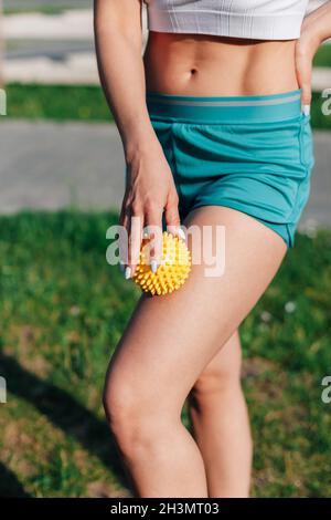 Spiky Gummi-Massage-Ball in den Händen der jungen Frau in Shorts für Cellulite-Reduktion und Gewichtsverlust auf Rasen im Garten am Sommermorgen Stockfoto