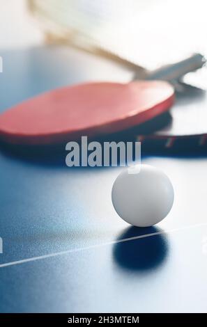 Zwei Tennisschläger und ein weißer Ball liegen auf einer Tischtennisplatte in der Nähe des Netzes. Aktive Erholung und Tischtennis spielen. Sporthintergrund. Stockfoto