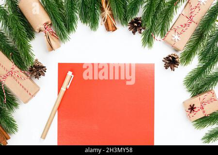 Imitierte rote leere Postkarten auf weißem Tisch im Rahmen von Christbaumzweigen mit Zapfen und Zimtbündel Stockfoto