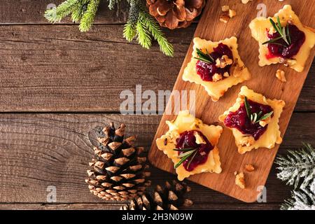 Weihnachtliche sternförmige Vorspeisen mit Preiselbeeren und gebratener Brie. Draufsicht auf einem Servierbrett vor einem Holzhintergrund. Speicherplatz kopieren. Stockfoto