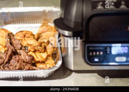 Luftfryer in der Küche. Kochen von Fleisch mit Gewürzen in einer Luftfryer. Selektiver Fokus auf Fleisch in Schale Stockfoto