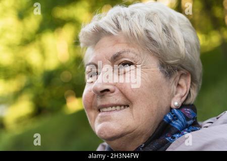 Porträt einer älteren Frau mit einem Blick in die Augen in den Park während der Herbstsaison. Blonde junge aussehende Dame mit positiv denkenden Blick Stockfoto