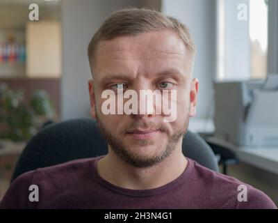 Person, deren Augen schief sind. Porträt des kaukasischen Mannes mit grauen Augen und Bart. Midlife Person mit Falten auf der Stirn Stockfoto