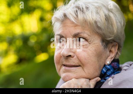 Porträt einer älteren blonden Frau mit der Hand am Kinn und dem Hoffnungslook. Lächelnde ältere Dame, die denkt, sie schaut seitwärts. Falten, Hautpflege, Copy Space Konzept Stockfoto