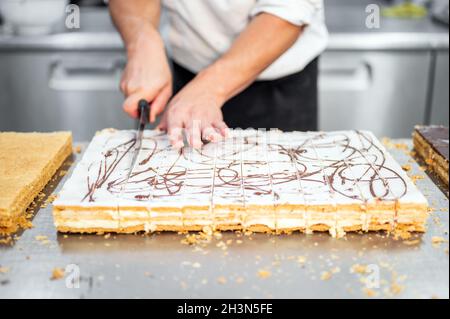 Nahaufnahme eines Konditors, der einen großen Kuchen in Portionen in der Konditorei schneidet. Stockfoto