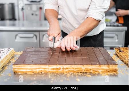 Nahaufnahme eines Konditors, der einen großen Kuchen in Portionen in der Konditorei schneidet. Stockfoto