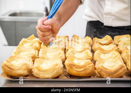 Der Konditormeister schmückt Biskuittartlet mit Creme aus der Tüte aus nächster Nähe Stockfoto