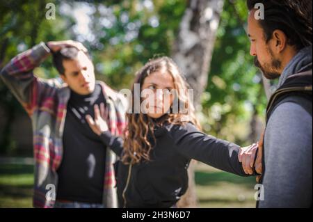 Die Frau versucht, die beiden aggressiven, wütenden, nervösen und verärgerten Männer im Streit zu trennen und steht mit ausgestreckten Armen zwischen ihnen. Gruppe quar Stockfoto