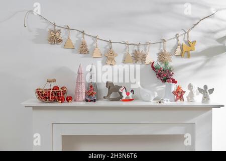 Dekoration des Innenraums der Wohnung zu Weihnachten. Eine Girlande aus geschnitzten Holzfiguren. Kerzen und Keramikfiguren auf einem künstlichen Kamin. Kopie en Stockfoto