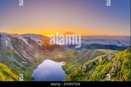 Erstaunlicher Sonnenaufgang auf dem Cadair Idris Berg in Snowdonia, Nordwales. Die Sonne scheint auf dem Gletschersee, die herrliche Wolkeninversion, die Berge umhüllt. Stockfoto