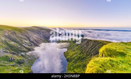 Erstaunlicher Sonnenaufgang auf dem Cadair Idris Berg in Snowdonia, Nordwales. Die Sonne scheint auf dem Gletschersee, die herrliche Wolkeninversion, die Berge umhüllt. Stockfoto